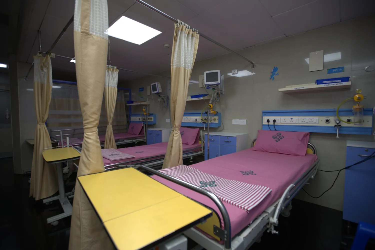 An empty PICU room with multiple beds with pink sheets separated by curtains.