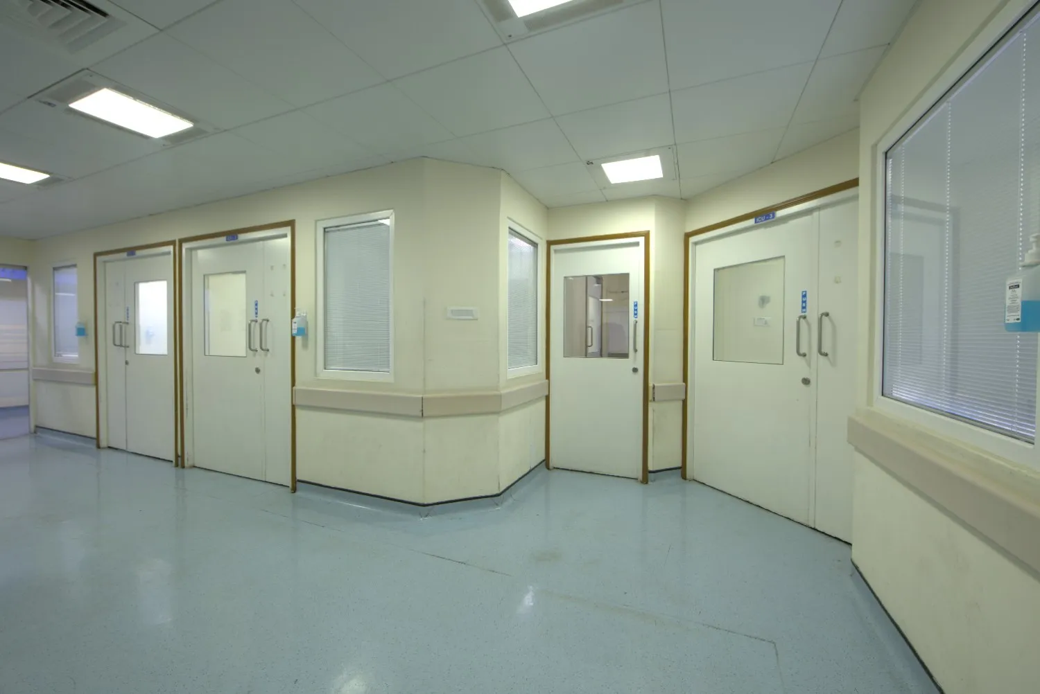 The exterior hallway of an ICU with white doors, viewing windows, and hand sanitizer dispensers.