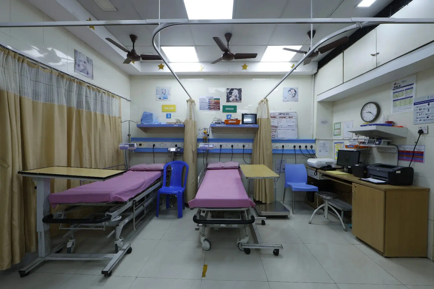 The empty pediatric emergency room at SMF Hospital in Anna Nagar with two beds and a desk.