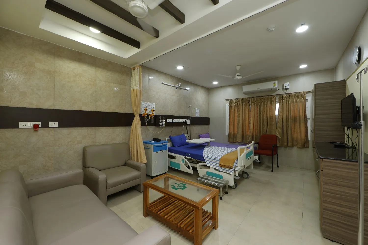 An empty inpatient room at SMF Hospital in Anna Nagar with a patient bed and visitor seating.