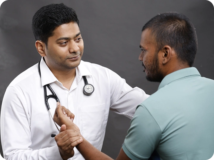 A masked doctor in a white coat uses a stethoscope to examine a male patient in a gray t-shirt